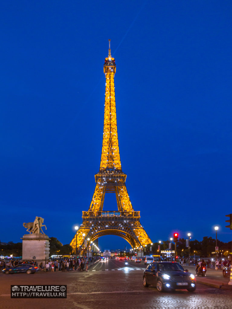 Illuminated Eiffel Tower as viewed from across Pont d'Iéna (Jena Bridge). You can also see the hourly baker's illumination in this shot. - Travelure ©